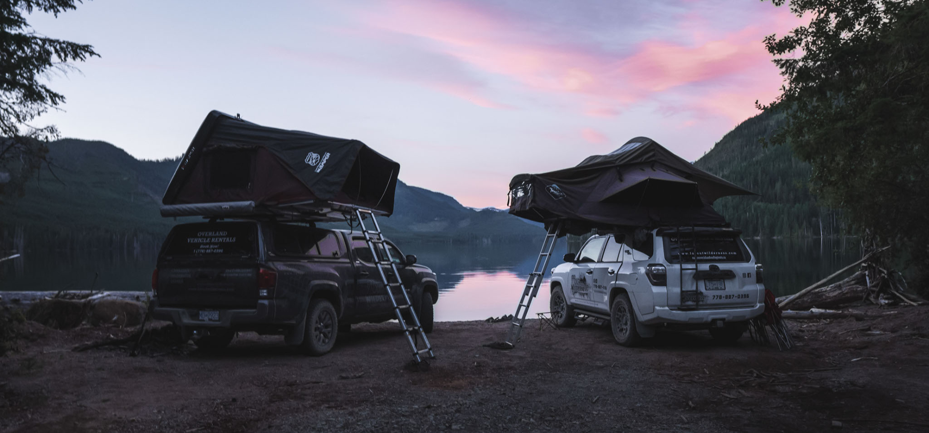 Two cars looking over lake with car tents on top of them with pink sunset.